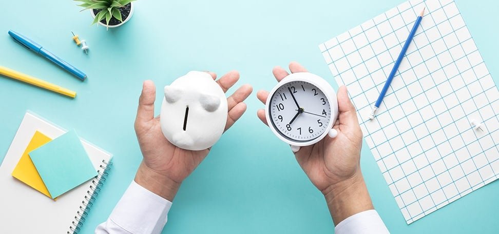 two hands over a desk with a piggy bank in one palm and clock in the other