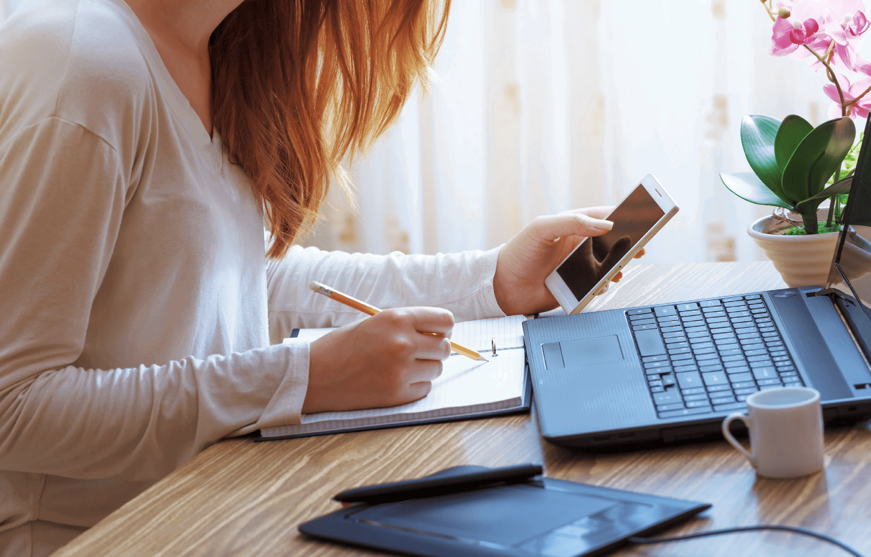 woman taking notes and looking at cellphone