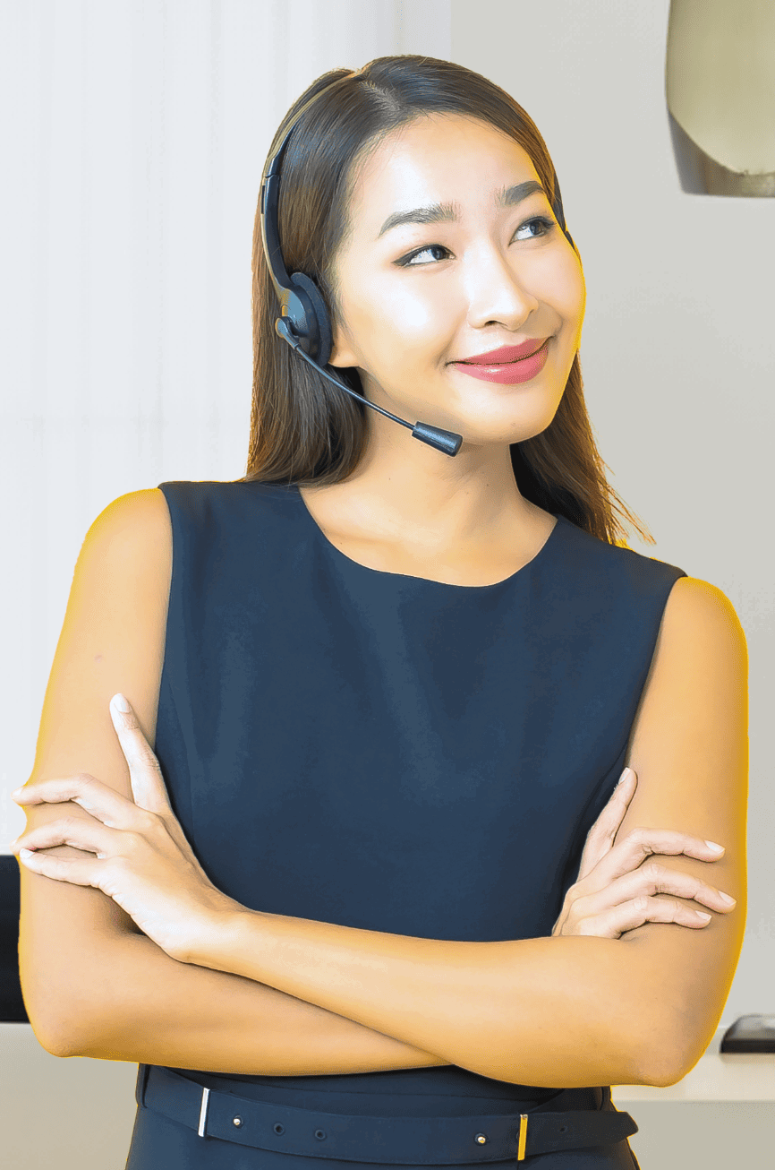 myoutdesk-loan-processor-virtual-assistant A woman wearing a black sleeveless dress and headset stands with her arms crossed, smiling slightly while looking to the side. She has long, straight hair and exudes the confidence of a loan officer assistant. The background is a softly lit indoor setting.