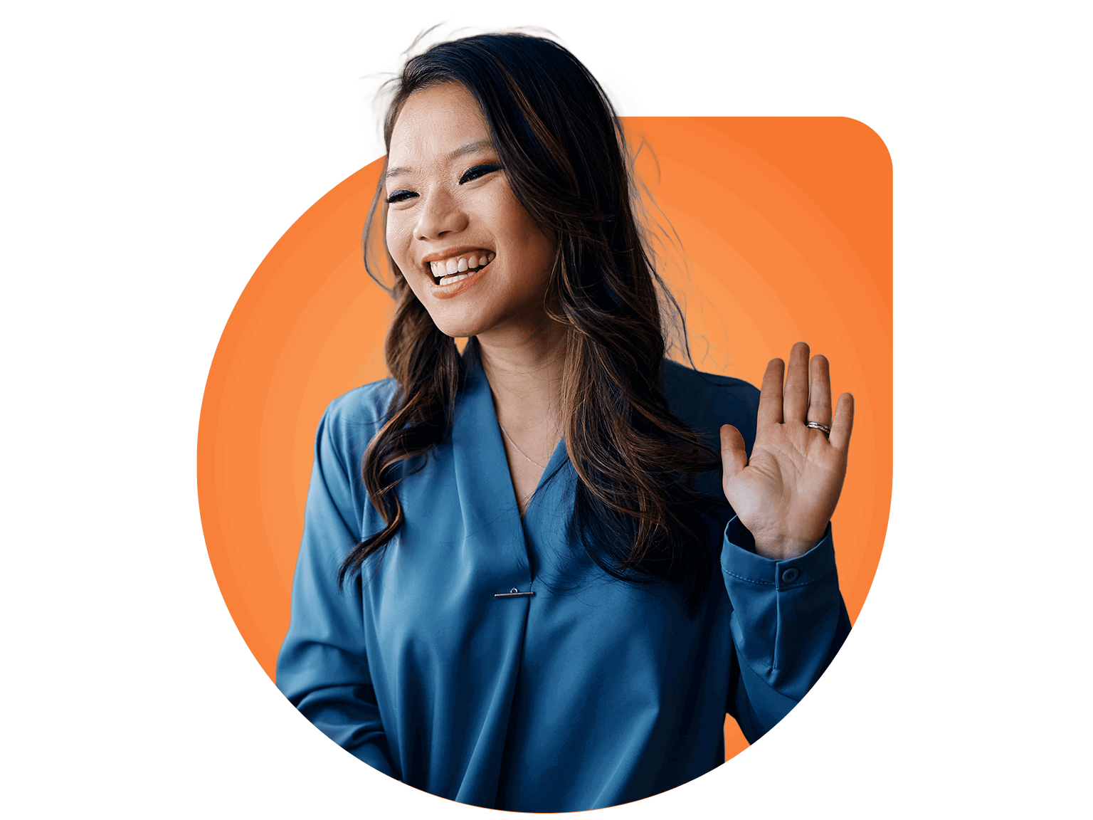 woman-waving-smiling-d-shape A smiling woman with long dark hair wearing a blue blouse raises her hand in a friendly gesture, standing in front of an orange background—ready to help as your Virtual Personal Assistant.